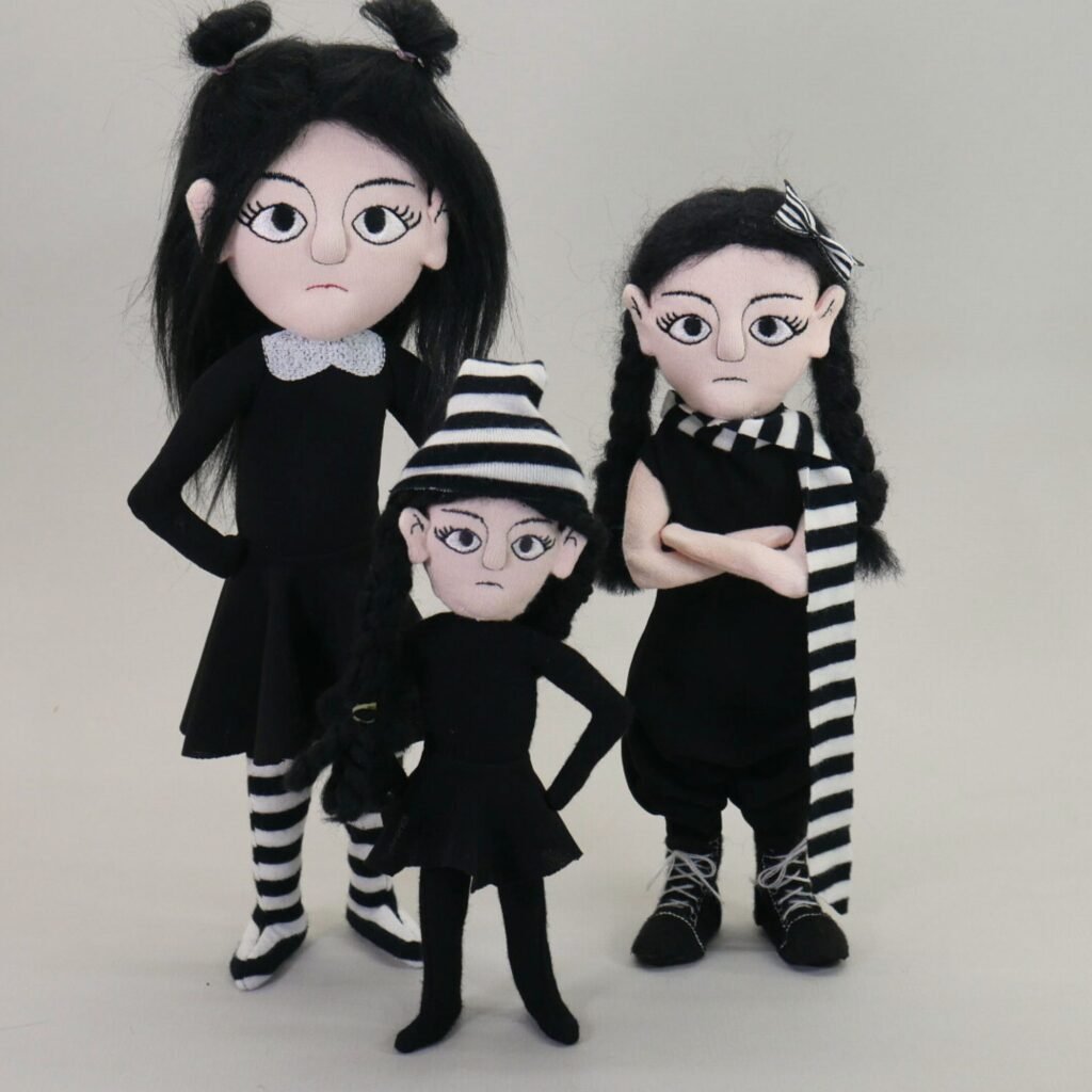 three little goth girl dolls in black clothes and striped accessories made in the hoop